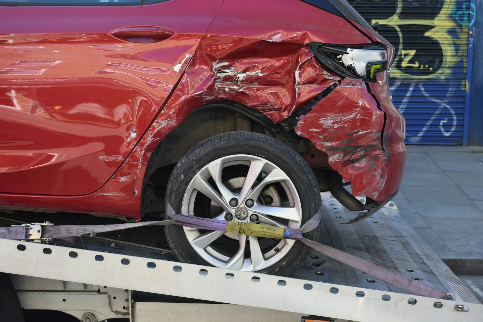 Red hatchback with a crushed rear door strapped onto a flatbed