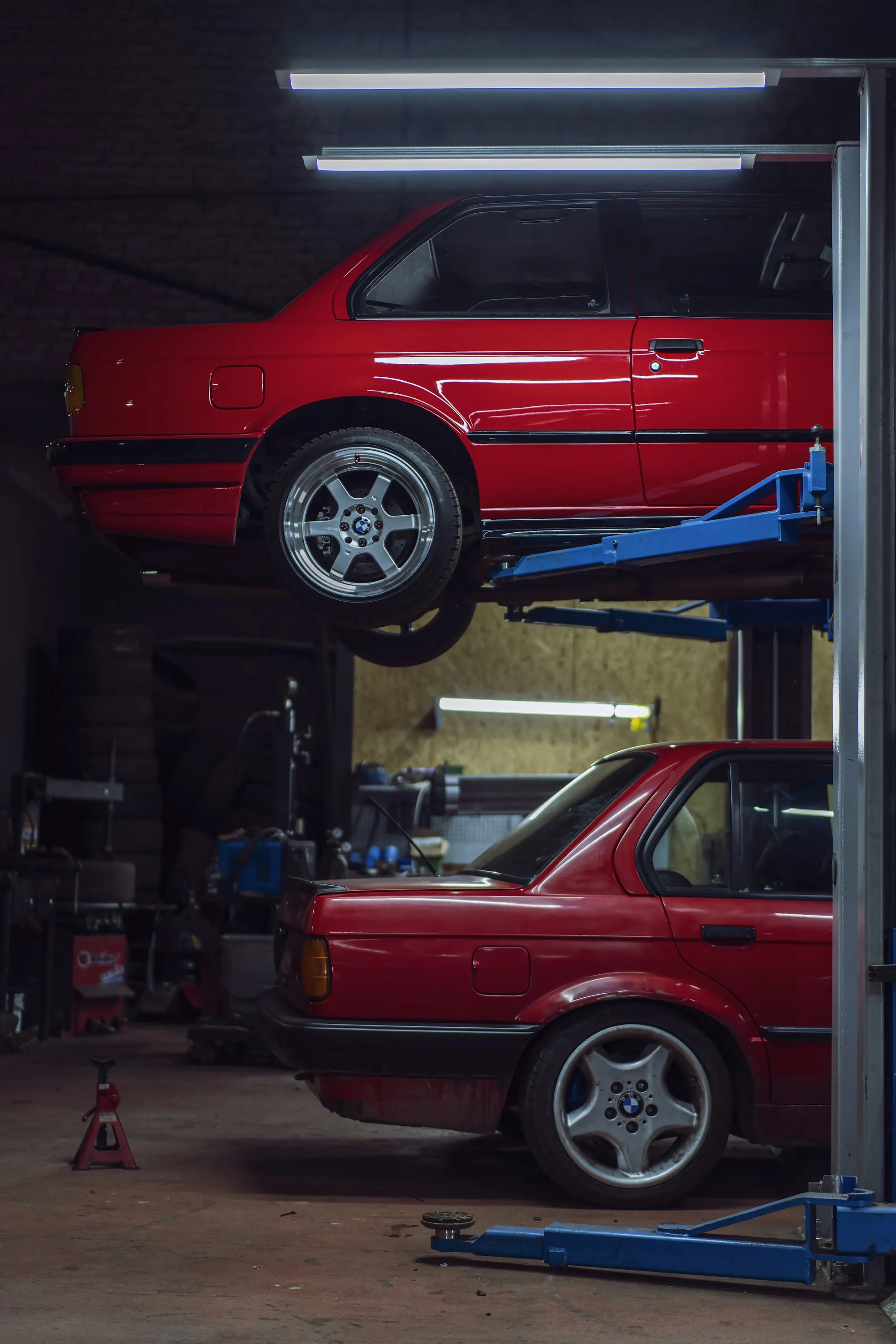 Two red cars raised on a stacked lift in a repair shop