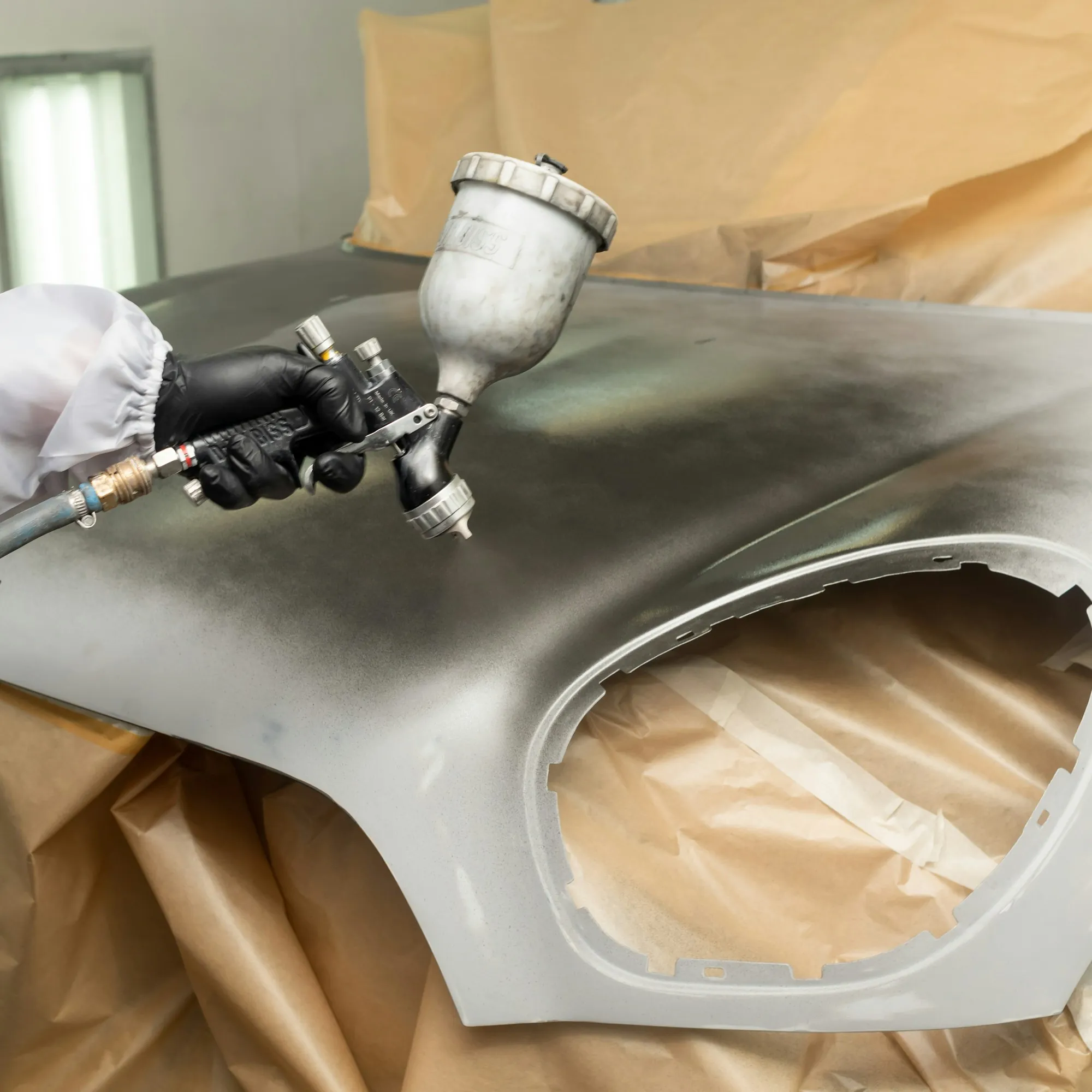 Spray gun applying paint to a car fender inside a masked-off booth